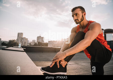 handsome sportsman stretching legs on roof during sunset Stock Photo