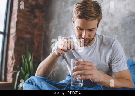 young man putting pill in glass of water in bed at home Stock Photo