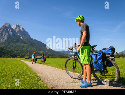 Cyclist on bike tour stands on bike path next to his mountain bike, in the back Zugspitze, Tegernauweg, near Grainau Stock Photo