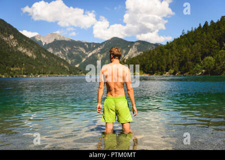 Young man bathing in Lake Plansee and looking into the mountains, shores, mountain lake, mountain landscape, Tyrolean Alps Stock Photo