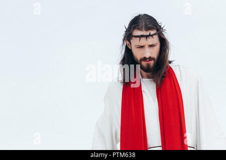 Jesus in robe, red sash and crown of thorns looking down against light sky Stock Photo