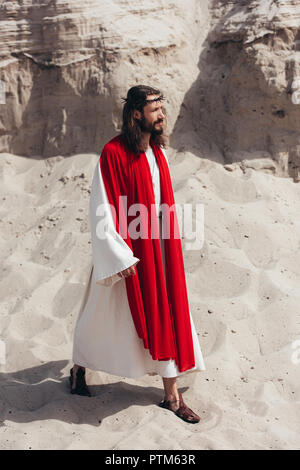 side view of Jesus in robe, red sash and crown of thorns walking in desert Stock Photo