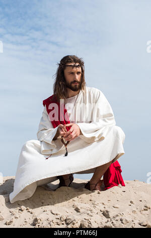 Jesus In Robe Red Sash And Crown Of Thorns Holding Rosary And Protecting  Face From Light In Desert Stock Photo - Download Image Now - iStock