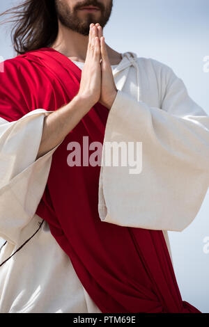 Jesus in robe, red sash and crown of thorns holding rosary and standing  with open arms against blue Stock Photo by LightFieldStudios