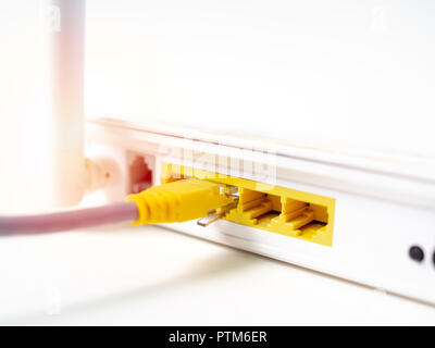 Close-up yellow ethernet cable connected on white wireless internet WI-FI router network hub isolated on white background. Stock Photo