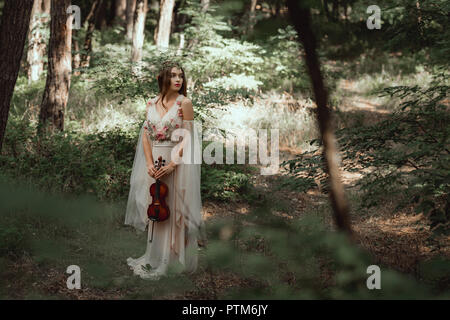 mystic elf in elegant dress holding violin in beautiful forest Stock Photo