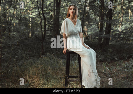 beautiful girl in white dress sitting on stool in forest Stock Photo