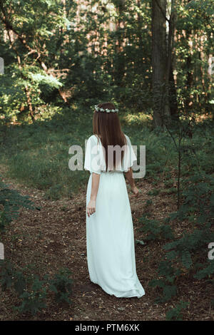 back view of girl in white elegant dress walking in forest Stock Photo