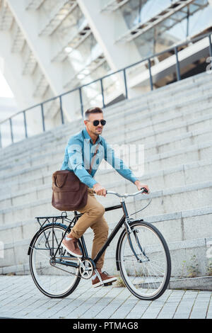handsome middle aged businessman in sunglasses riding bike on street Stock Photo