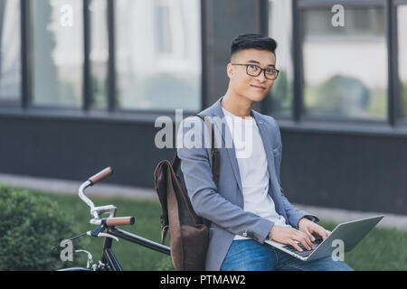 smiling asian teleworker using laptop while sitting on bicycle Stock Photo