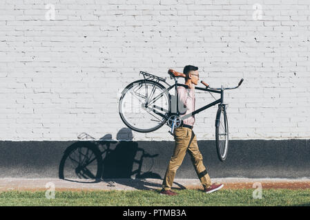 side view of asian man carrying bicycle while walking on street Stock Photo
