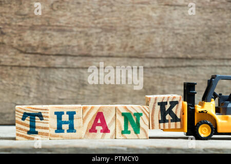 Yellow toy forklift hold letter block K to complete word thank on wood background Stock Photo