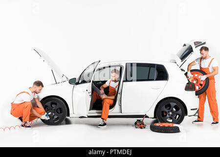 handsome auto mechanic inflating tire, using laptop and taking tire on white Stock Photo