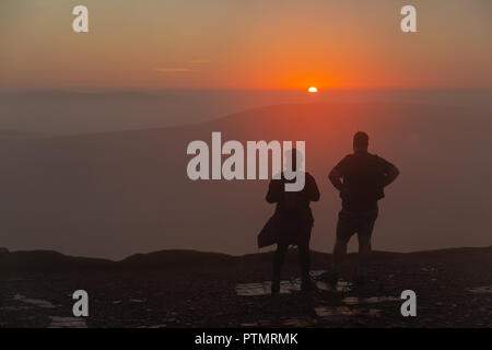 Pen y Fan, Brecon Beacons, Wales, UK. 10th October 2018. Hill walkers enjoy a dramatic sunrise from the peak of Pen y Fan, the highest mountain in southern Britain located in the Brecon Beacons.  On what is forecasted to be a warm and bright autumnal day with temperatures in south Wales predicted to peak over 21degrees celsius. Credit: Haydn Denman/Alamy Live News Stock Photo