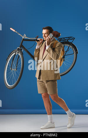 smiling man carrying bicycle and talking by smartphone on blue Stock Photo