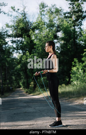 sportswoman exercising with jump rope on path in park Stock Photo