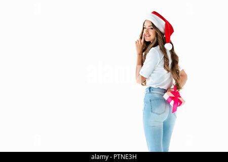 attractive girl in santa hat hiding christmas present and showing silence symbol, isolated on white Stock Photo