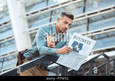 shocked middle aged man holding coffee to go and reading business newspaper Stock Photo