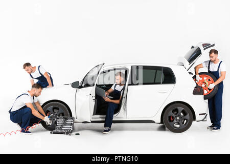 handsome auto mechanic inflating tire, using laptop and holding tire on white Stock Photo