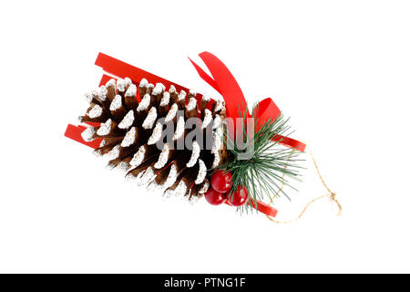 Giant Christmas pine cone decorated with silver glitter, bell and red ribbon on red wooden sledge isolated on white background. Stock Photo