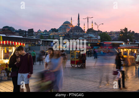 Eminonu bazaar with food stalls and people with Suleymaniye mosque lit up in the background at sunset, Istanbul, Turkey Stock Photo