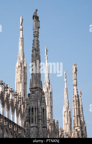 Photo taken high up on the terraces of Milan Cathedral / Duomo di Milano, Italy, showing the gothic architecture in detail against a clear blue sky.
