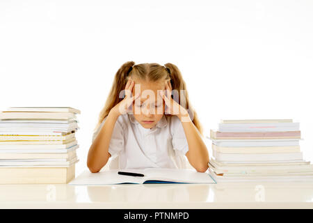 Sad and tired cute schoolgirl with blond hair sitting in stress doing homework overwhelm with too much study and textbooks in children education acade Stock Photo