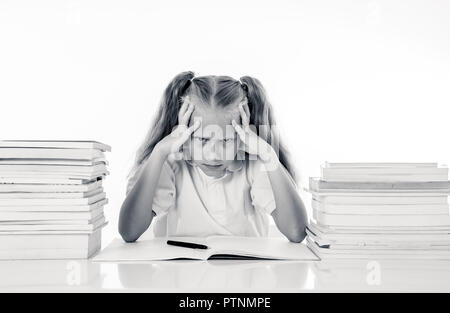 Sad and tired cute schoolgirl with blond hair sitting in stress doing homework overwhelm with too much study and textbooks in children education acade Stock Photo