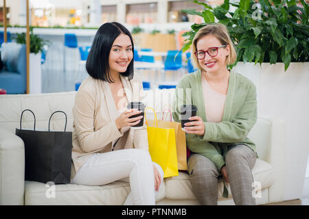 Two young women having coffee break together at shopping mall Stock Photo
