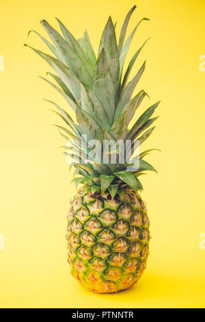 A whole, fresh pineapple with textured and patterned skin on a yellow background Stock Photo