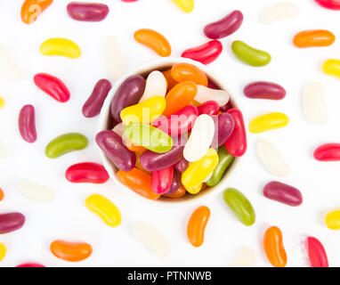 Looking down from above onto a bowl full of colourful jellybeans and candy scattered over a white background Stock Photo