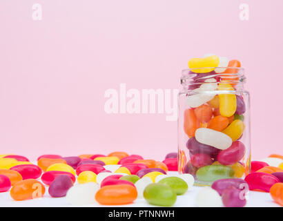 A glass jar full of chewy jelly bean candy in a sweet shop with a pink background and copy space Stock Photo