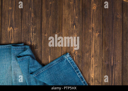 Frayed jeans or blue jeans denim collection on rough dark wooden table background, top view with copy space, old fashion style concept. Stock Photo