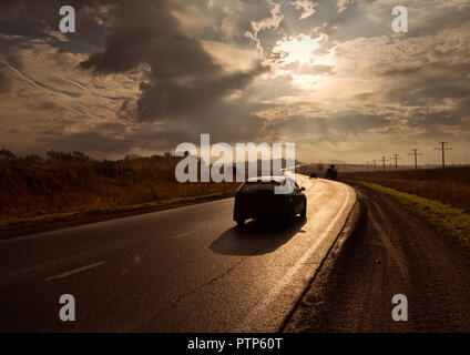 sunset road glistens in the sun strives forward. lonely car on a highway Stock Photo