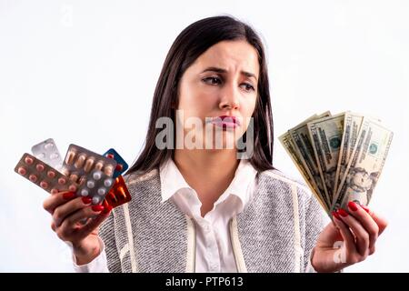 Different colorful pills and capsules in blisters in the hands of beautiful young woman. Looking at the money. Studio shot isolated on a white backgro Stock Photo