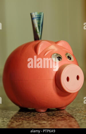 Pig plastic piggy bank with note in slot representing saving Stock Photo