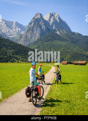Three cyclists on bike tour are on bike path, in the back Zugspitze, Tegernauweg, near Grainau, crossing the Alps Stock Photo