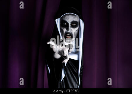 closeup of a frightening evil nun, wearing a typical black and white habit, peeping out from a purple curtain Stock Photo