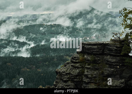 Deadpan dark misty rainy morning landscape with the sand rocky montains in Czech Saxon Switzerland in autumn colors. Stock Photo