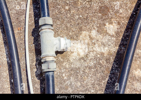 Few black plastic water hoses with bifurcation part are placed on concrete floor. Stock Photo