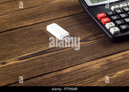 White USB flash drive and calculator on a wooden background, close-up Stock Photo