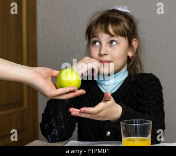 The mother holds out the apple to the girl who goes to school, schoolgirl Stock Photo