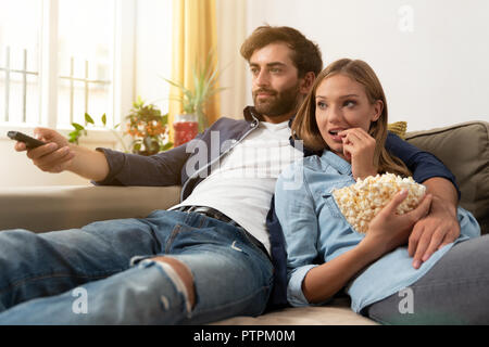 Couple watching TV, eating popcorn on a sofa at home Stock Photo