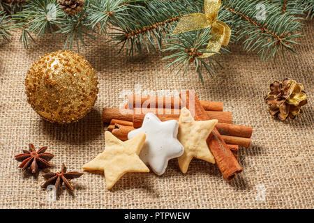 Christmas gingerbread cookies on sackcloth with cinnamon, star anise, glittering ball and natural fir tree branches with cones Stock Photo