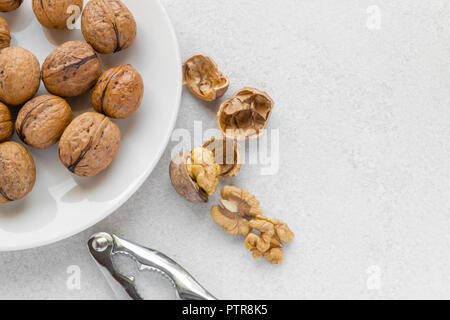 Whole walnuts on a plate, metal nutcracker and cracked walnuts next to Stock Photo