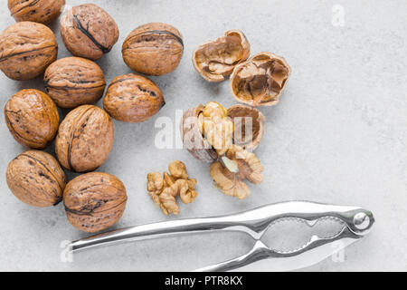 Whole and cracked walnuts next to silver nutcracker on white background Stock Photo