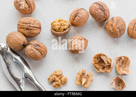 Whole and cracked walnuts next to silver nutcracker on grey background Stock Photo
