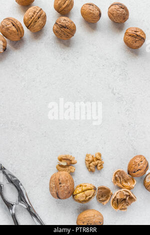 Whole and cracked walnuts, silver nutcracker and copy space in the middle on white background Stock Photo