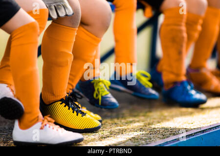 Footballers in soccer cleats. Youth athletes in soccer clothes. Young football players wearing football clothes and soccer shoes sitting on bench in a Stock Photo