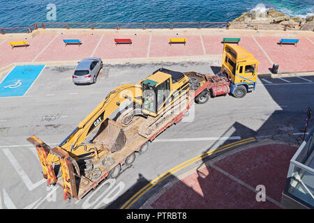 XGHAJRA, MALTA - OCTOBER 5, 2018: Large trailer transports excavator from construction site through narrow streets of Malta, top view Stock Photo